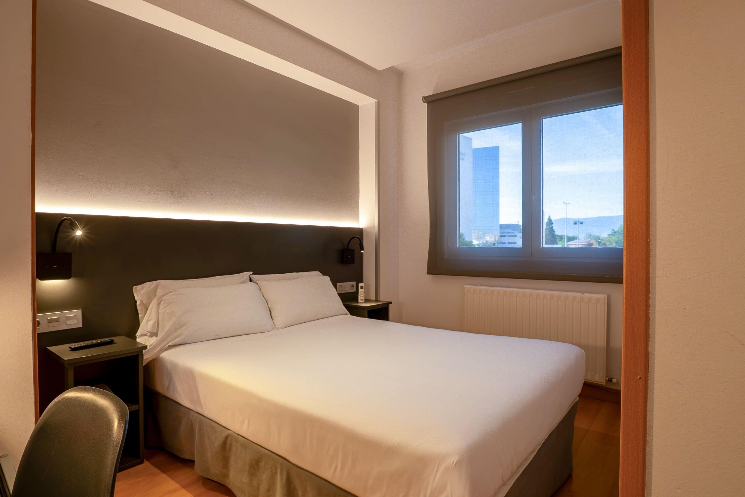 Une chambre d’hôtel équipée d’un lit, de tables de chevet, d’une chaise, d’une fenêtre avec vue et d’un téléviseur fixé au mur.