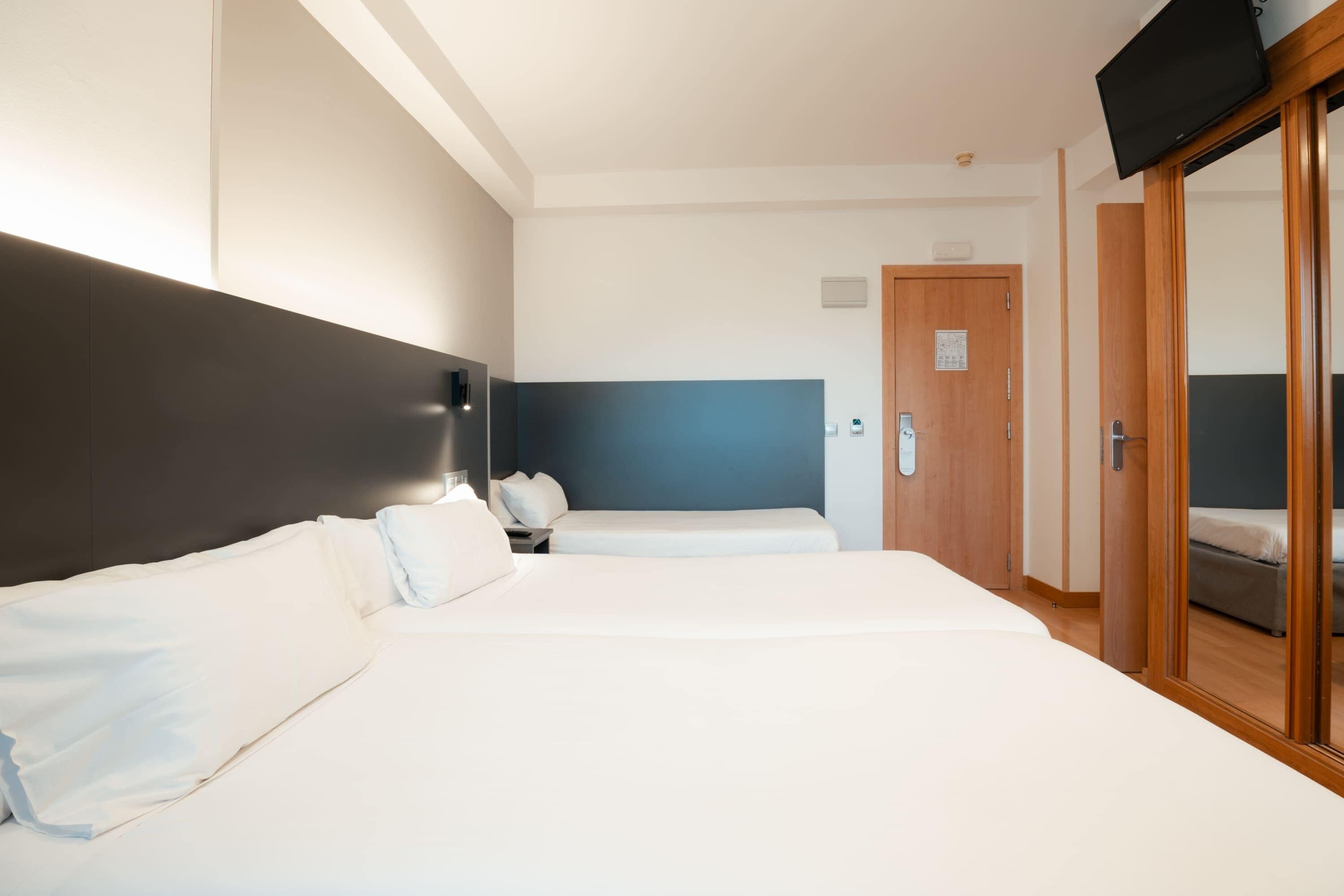 Ein Hotelzimmer mit zwei Betten, einem an der Wand befestigten Fernseher und einem Holzschrank.