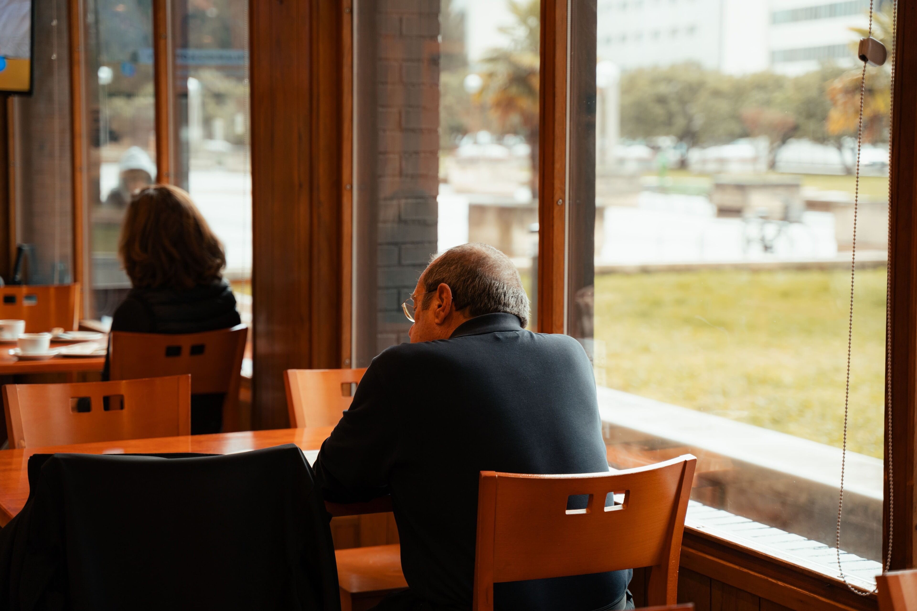 A man and a woman sitting at a wooden table in a restaurant with large windows.