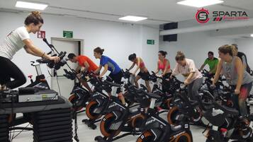 A group of people exercising on stationary bikes in a gym with a white wall and a door in the background.