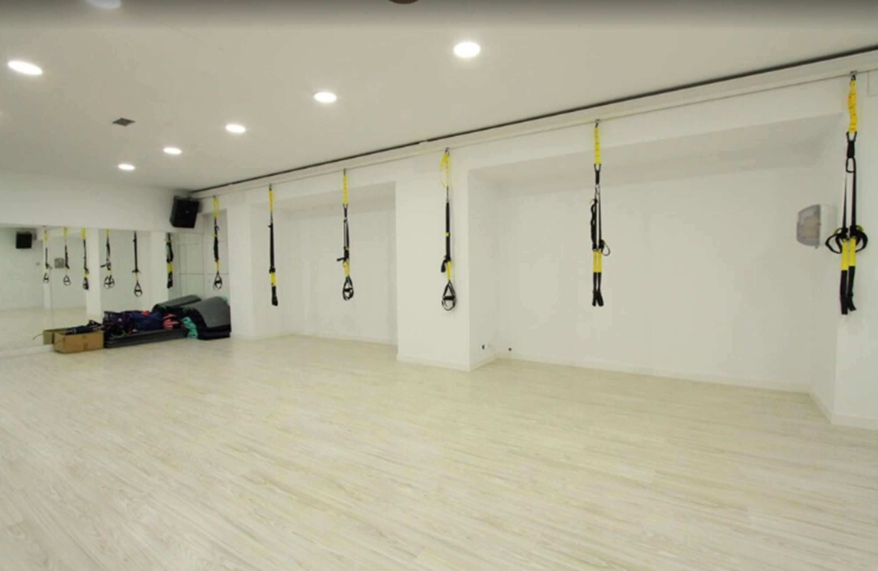 A spacious room with white walls and a wooden floor, equipped with multiple TRX suspension straps for exercise.