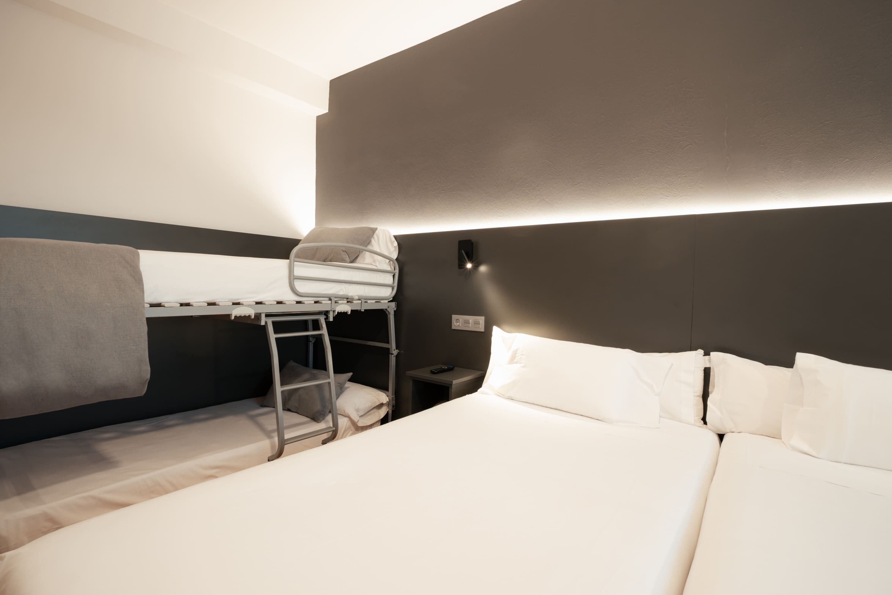 A hotel room with a bunk bed, a bedside table, and a wall-mounted light.