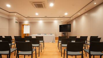 A conference room with rows of chairs, a whiteboard, a table with water bottles, and a TV screen.