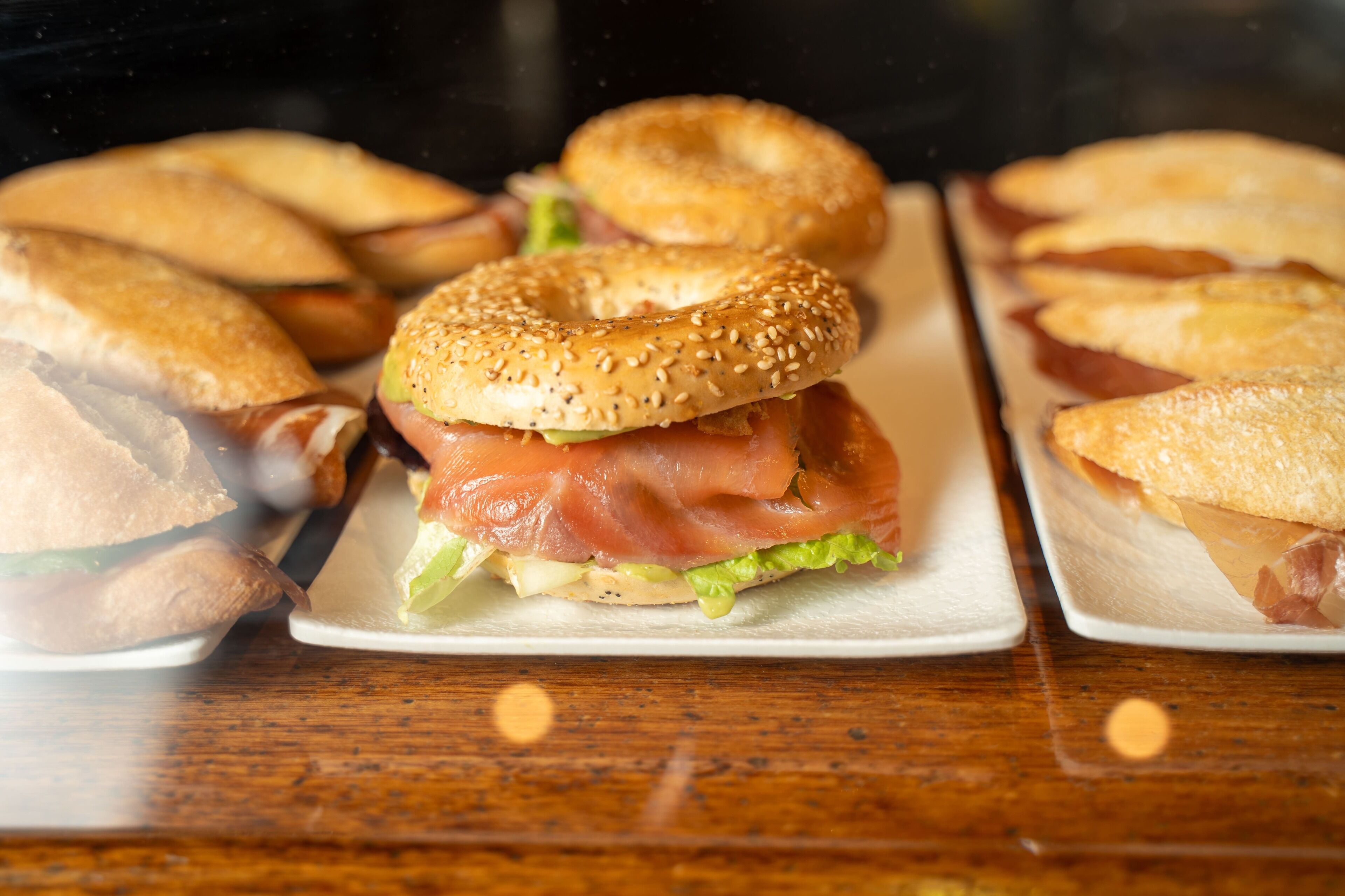 Sándwiches de pan con semillas de sésamo y salmón ahumado sobre una mesa de madera.