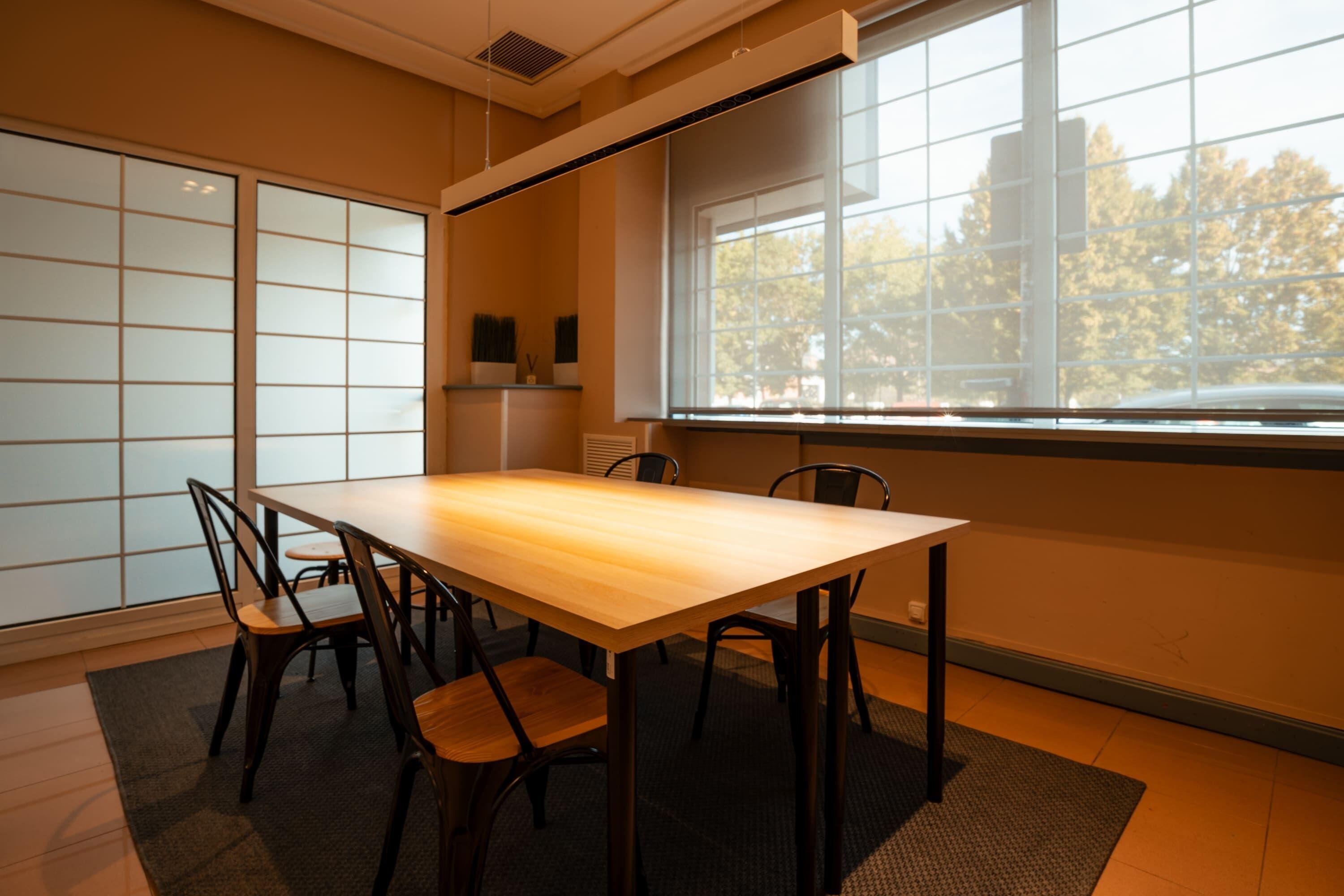 A conference room with a wooden table and chairs, large windows with a view of trees, and a traditional Japanese shoji screen.