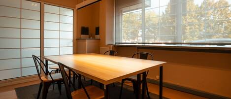 A conference room with a wooden table and chairs, large windows with a view of trees, and a traditional Japanese shoji screen.