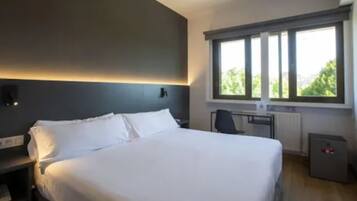 Una habitación de hotel moderna con una cama grande, un escritorio y una ventana con persianas.