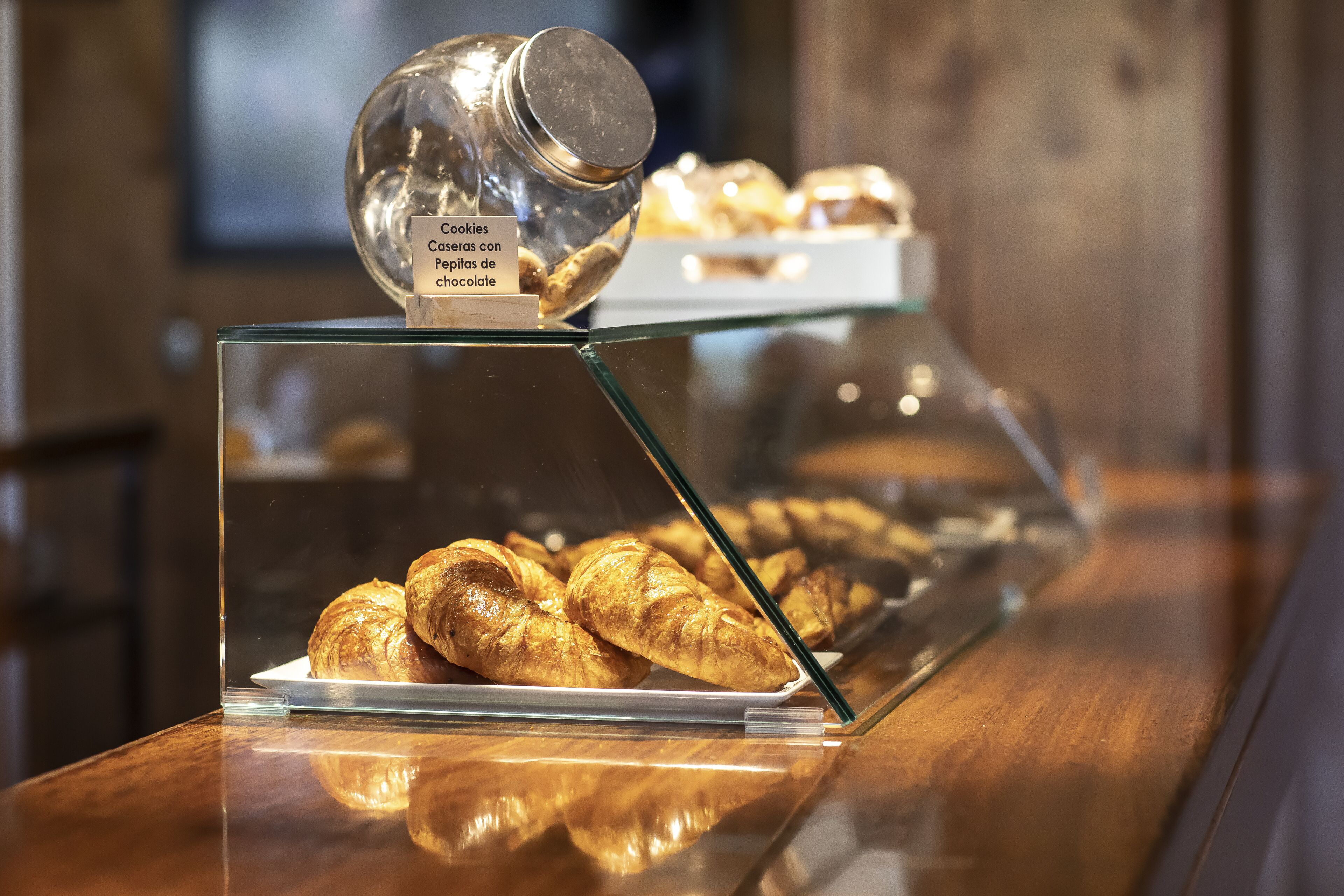 Una vitrina con pasteles y un tarro etiquetado como 'Cookies Caseras con Pepitas de chocolate'.