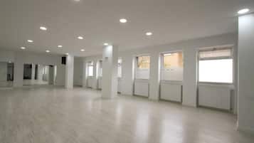 A spacious, well-lit room with a wooden floor, large windows, and ceiling lights.
