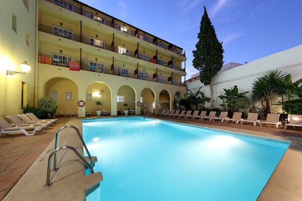 Una piscina con sillones de descanso y un edificio con balcones.