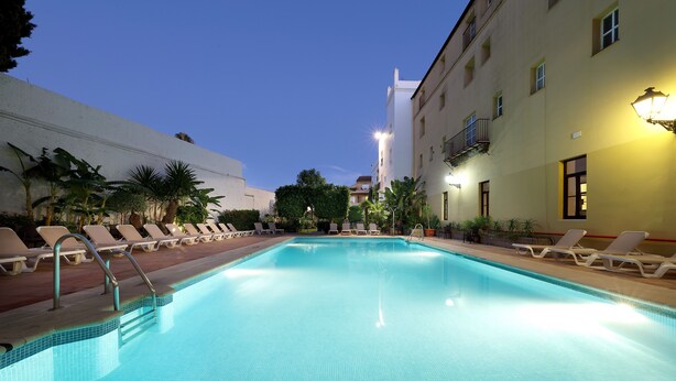 A swimming pool with sun loungers and a building in the background.