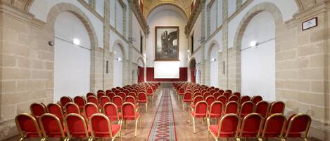 A conference room with rows of red chairs, a central aisle, and a large painting on the back wall.