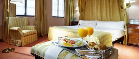 A hotel room with a bed, a chair, a tray with breakfast, and a window with curtains.