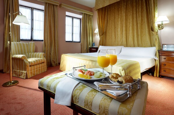 A hotel room with a bed, a chair, a tray with breakfast, and a window with curtains.