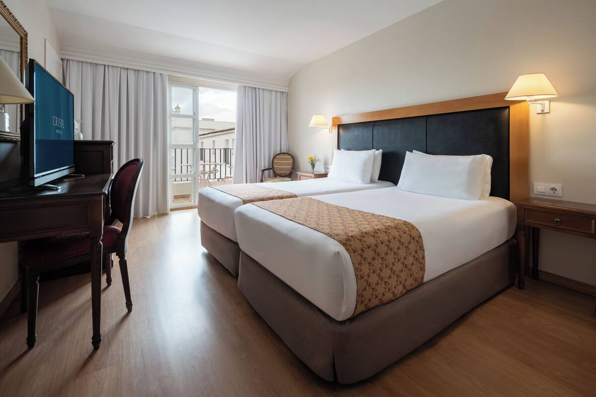 A hotel room with two beds, a desk, a chair, a TV, and a balcony.