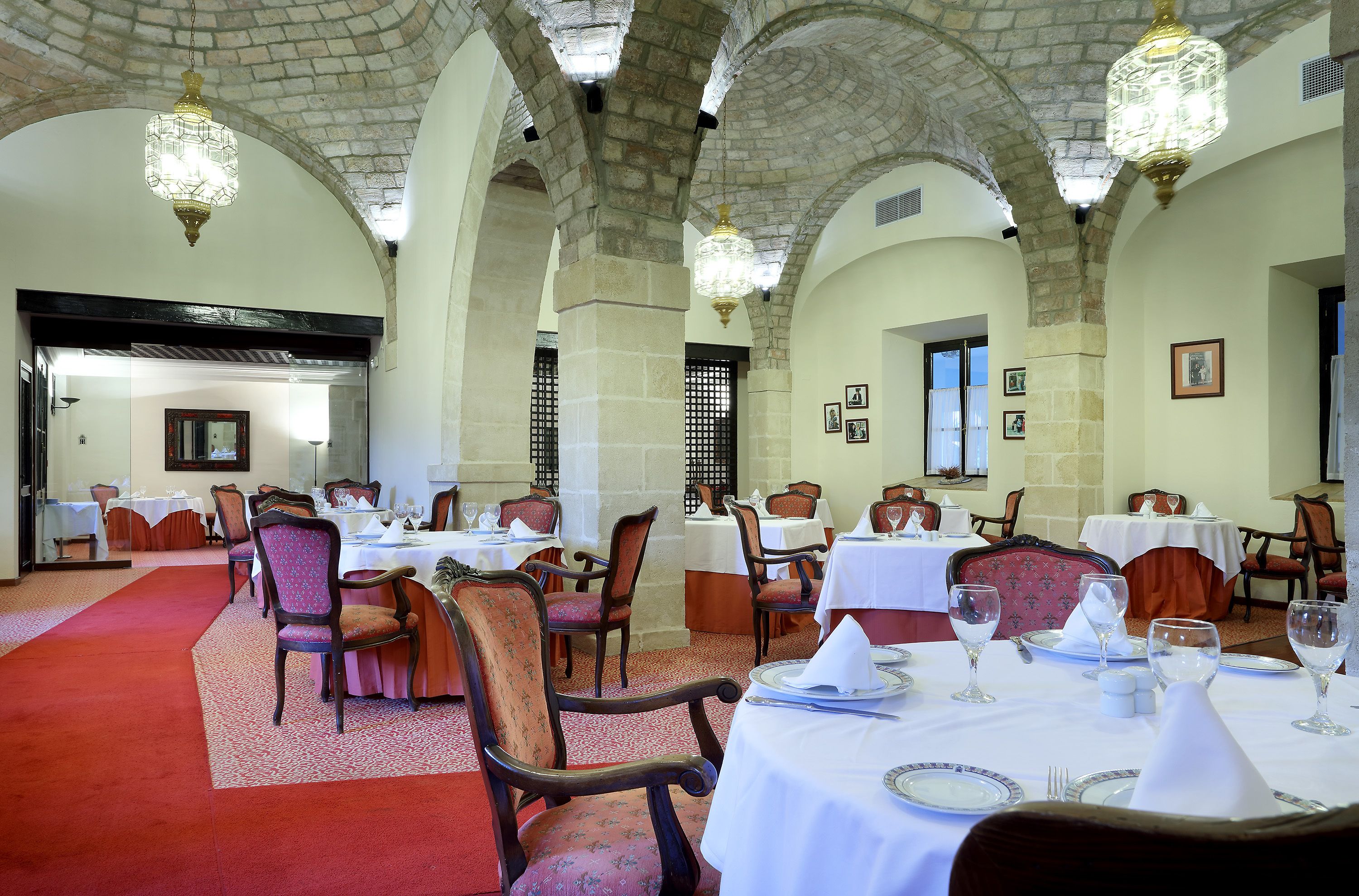 A dining area with tables set for service, stone arches, and chandeliers.