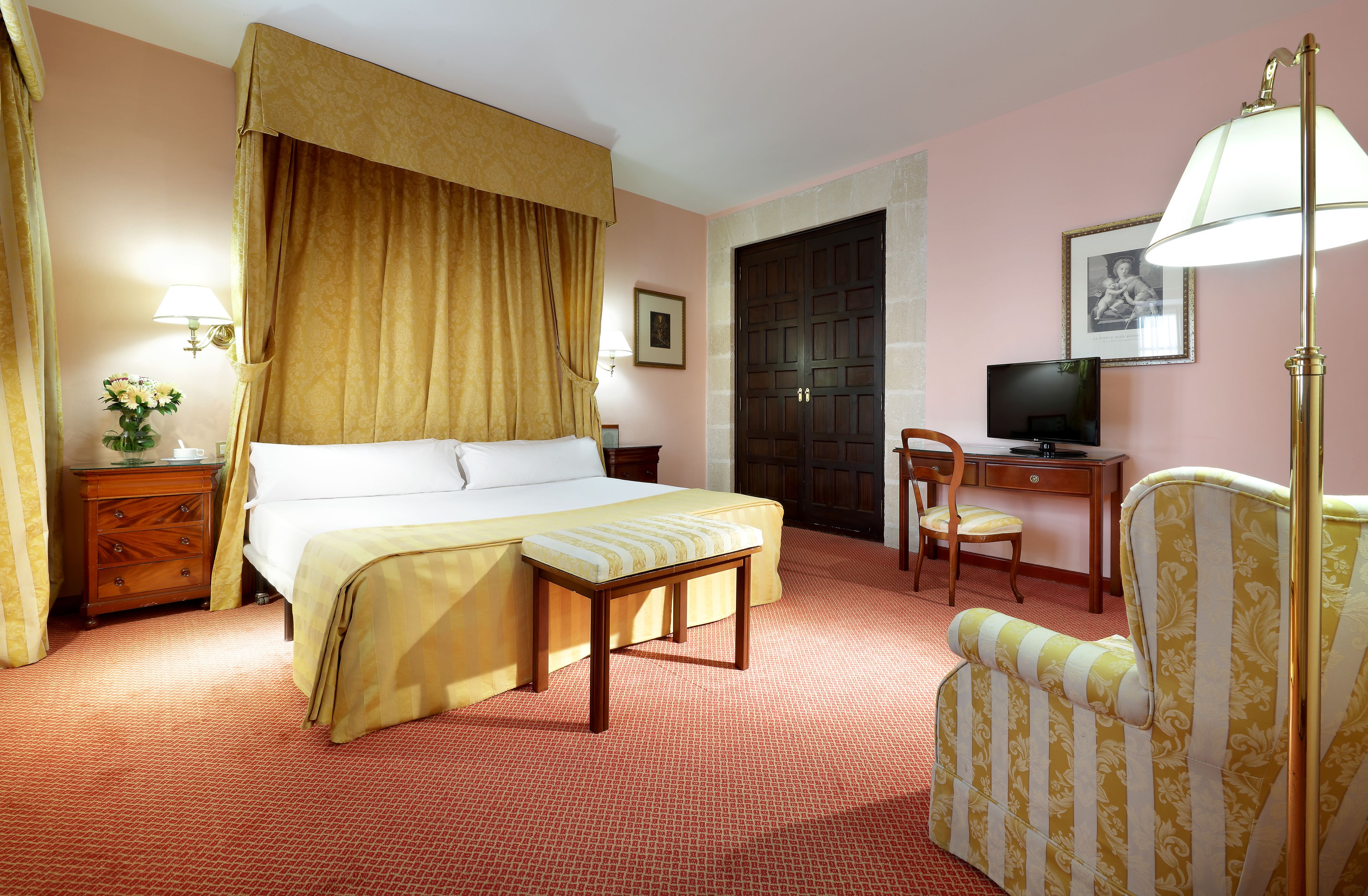 Una habitación de hotel con una cama grande, un escritorio con silla, televisión y una lámpara.