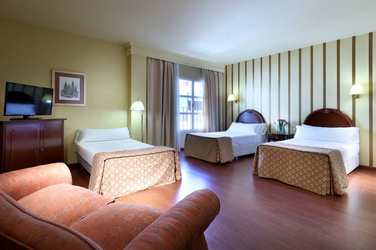 A hotel room with two beds, a sofa, a TV, and a window with curtains.