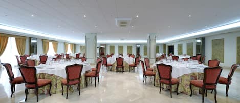 Un amplio salón de conferencias con múltiples mesas redondas, cada una con sillas y manteles blancos.