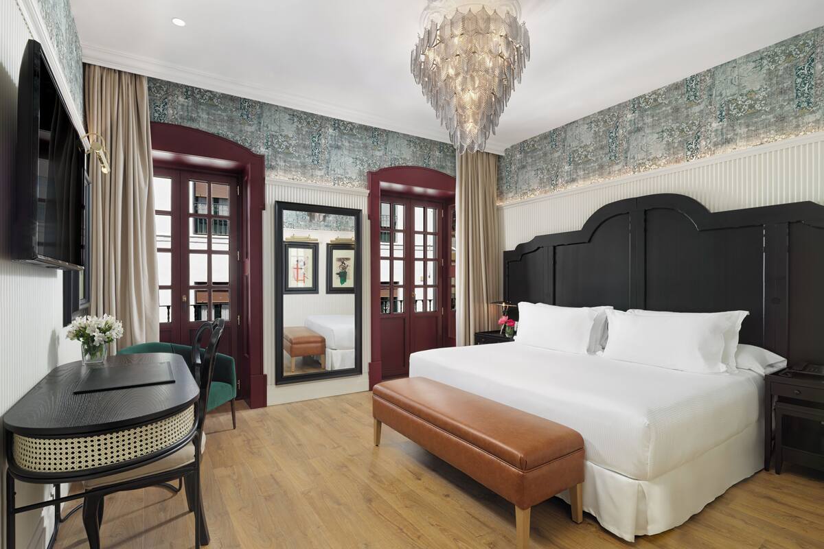 A spacious bedroom with a large bed, a bench, a desk, and a chandelier.
