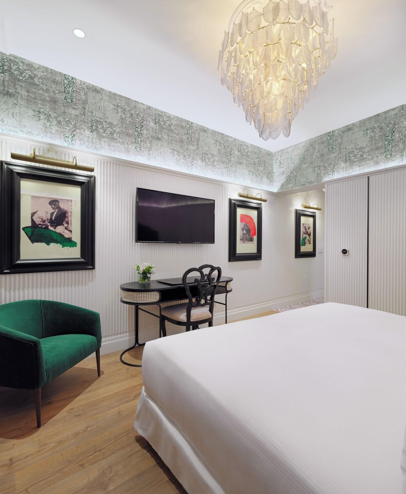A bedroom with a large bed, a desk with a chair, a television, and framed pictures on the wall.