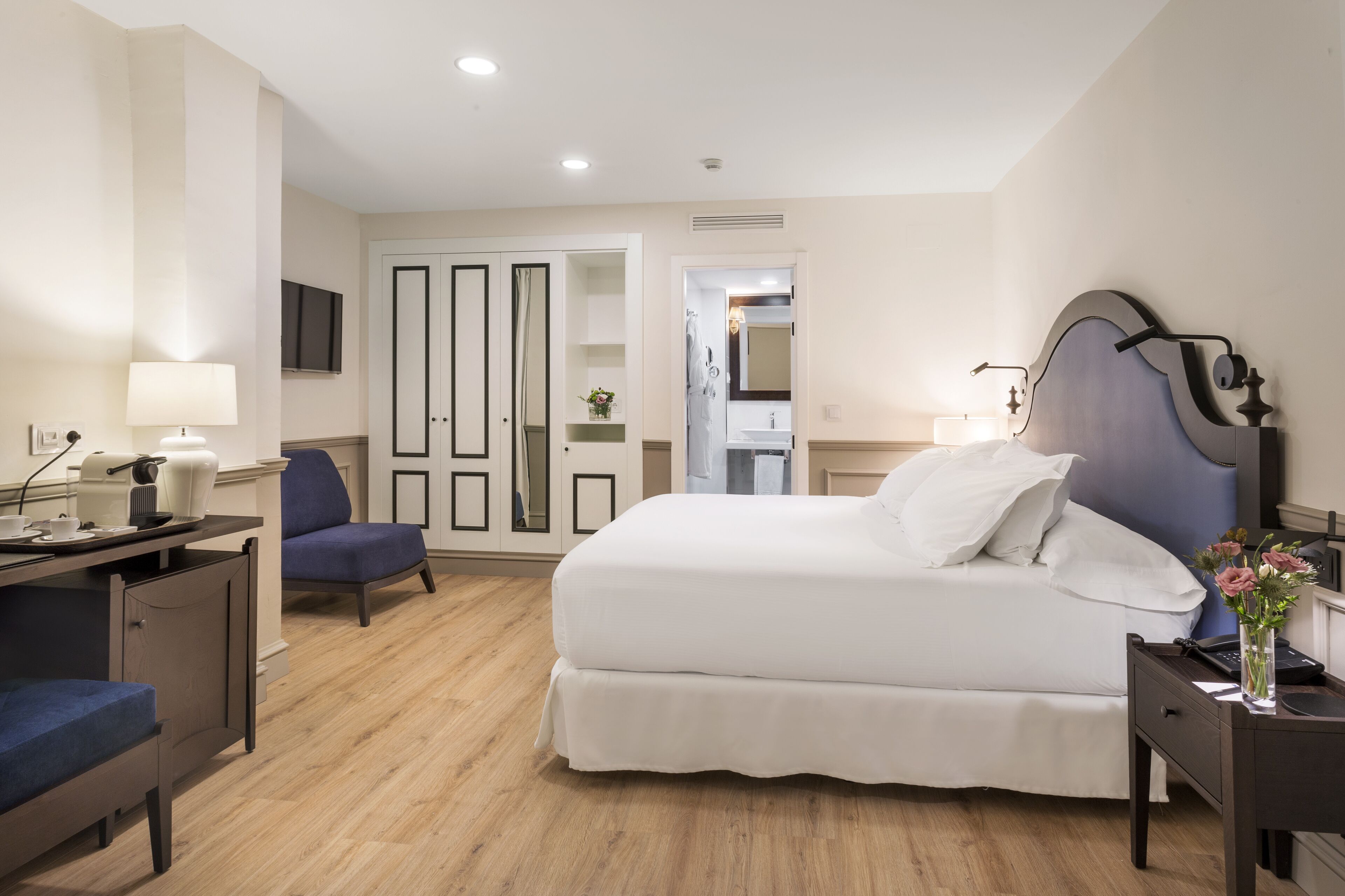 A hotel room with a bed, a desk, a chair, a wardrobe, and a bathroom visible through an open door.