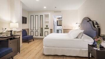 A hotel room with a bed, a desk, a chair, a wardrobe, and a bathroom visible through an open door.