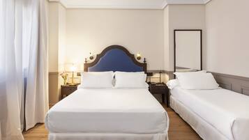 Habitación de hotel con dos camas individuales, una mesita de noche con lámpara, un espejo y una ventana con cortinas.