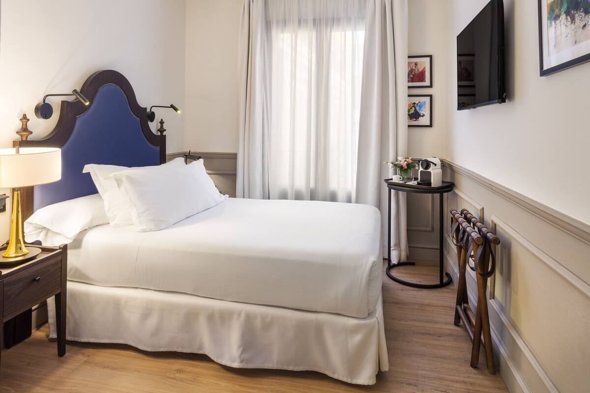 A neatly made bed with white linens, a bedside lamp, and a headboard.