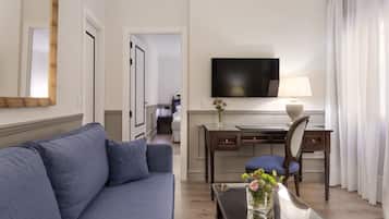 Een hotelkamer met een blauwe bank, een bureau met een stoel, een flatscreen televisie en een vaas met bloemen.