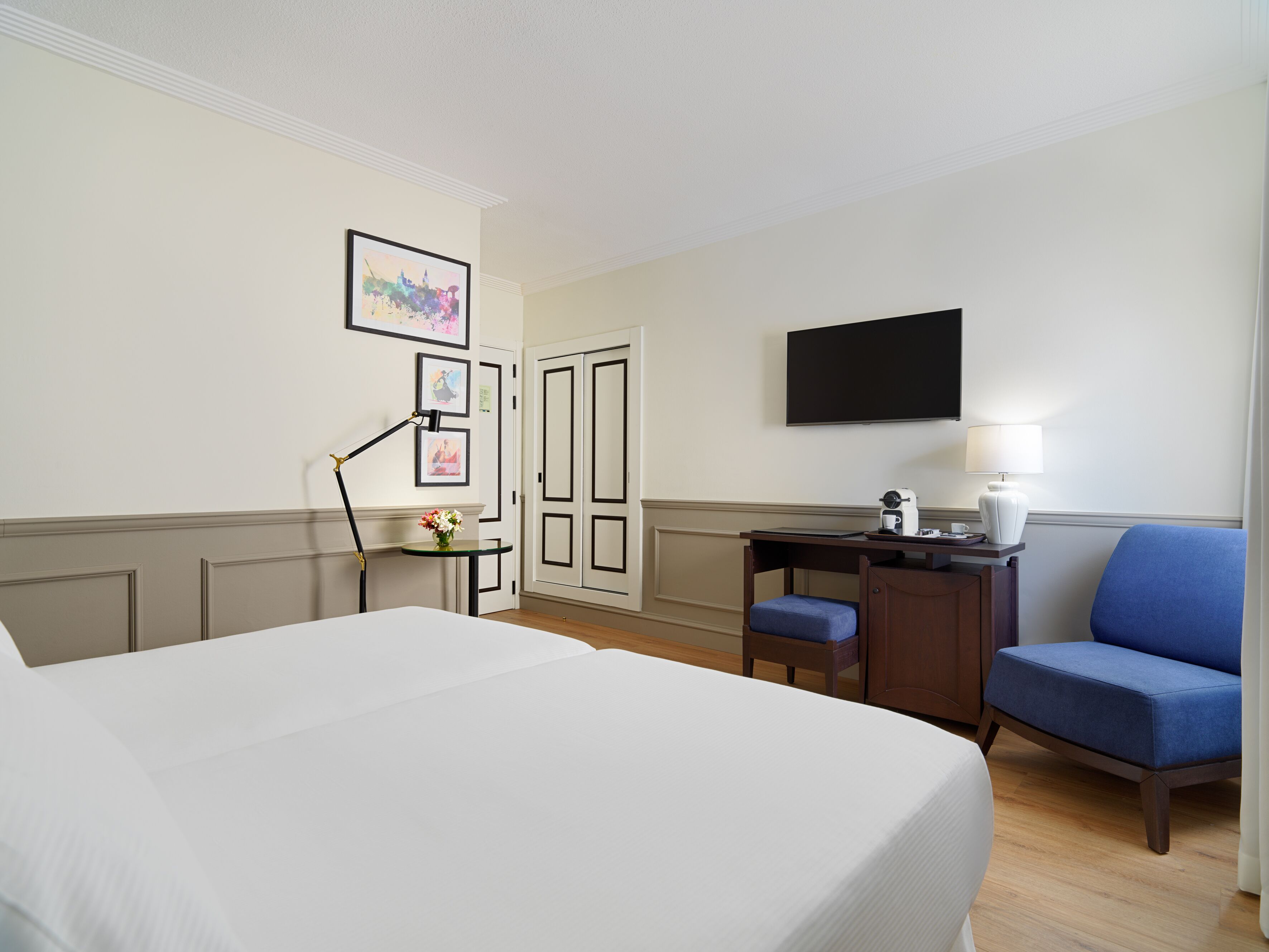 Una habitación de hotel con cama, escritorio, silla, televisión y lámpara.