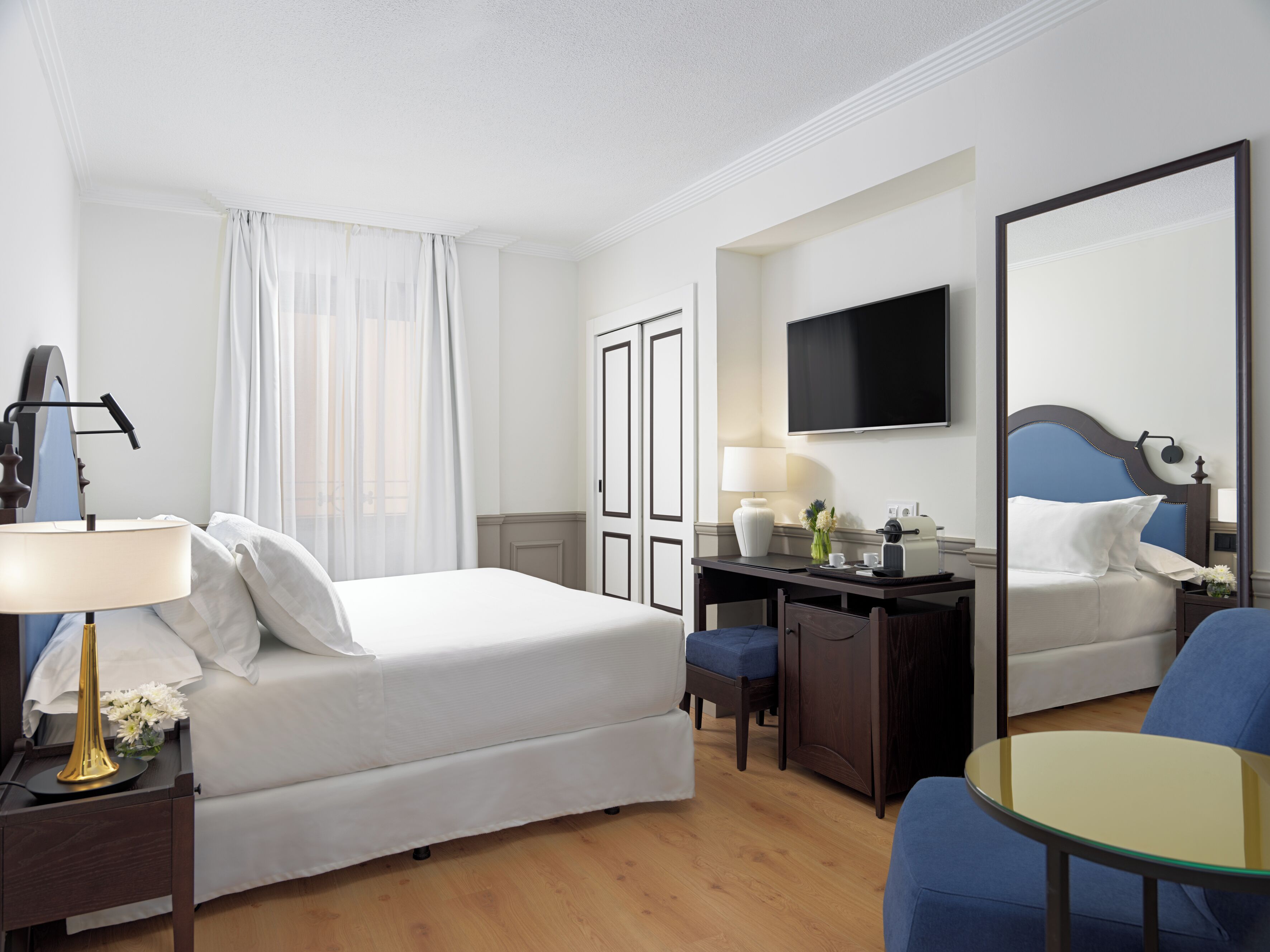 A hotel room with a bed, desk, chair, and a large mirror.