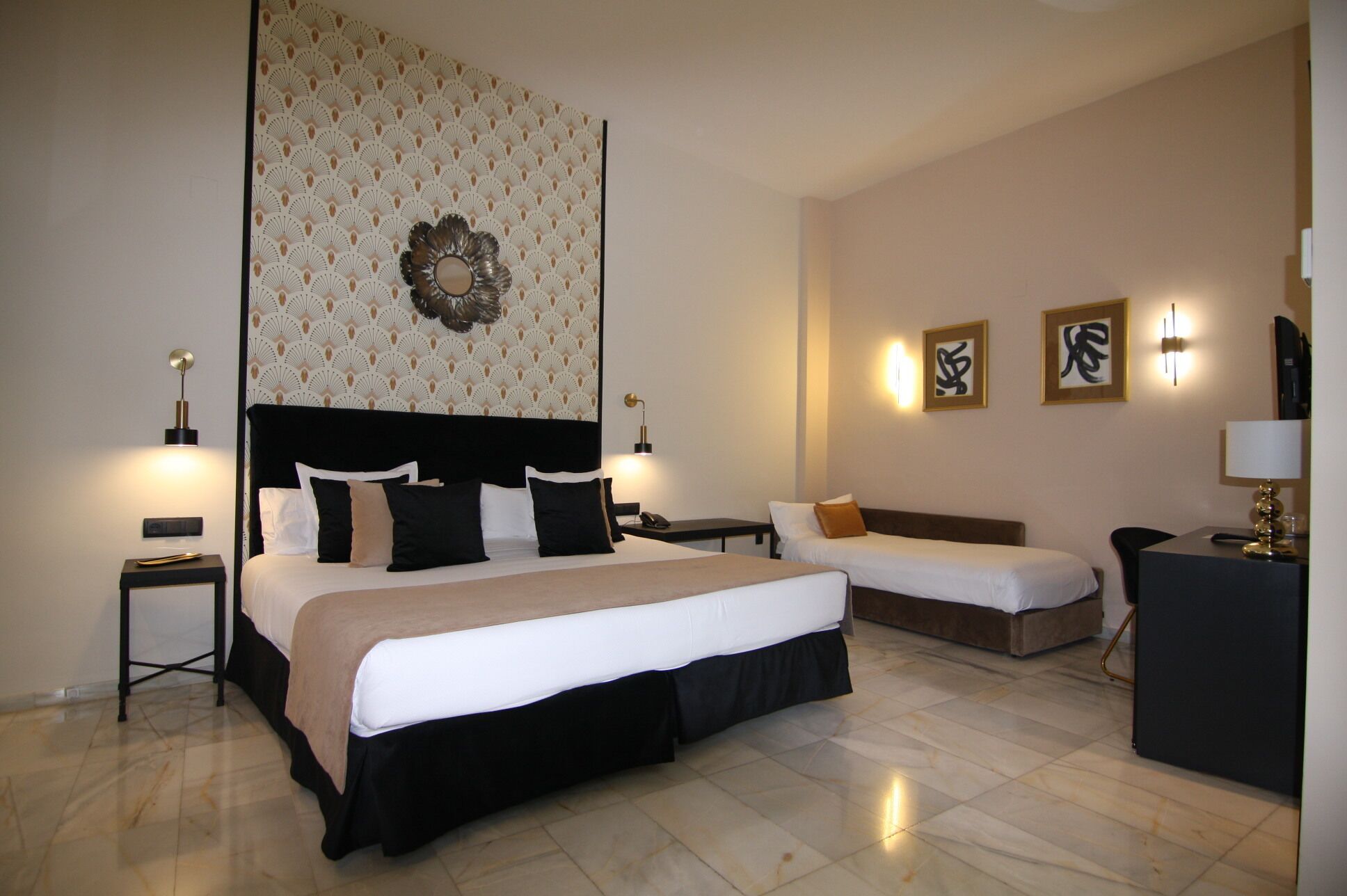 A hotel room with a large bed, a smaller bed, two bedside tables, a desk, and a decorative wall piece.