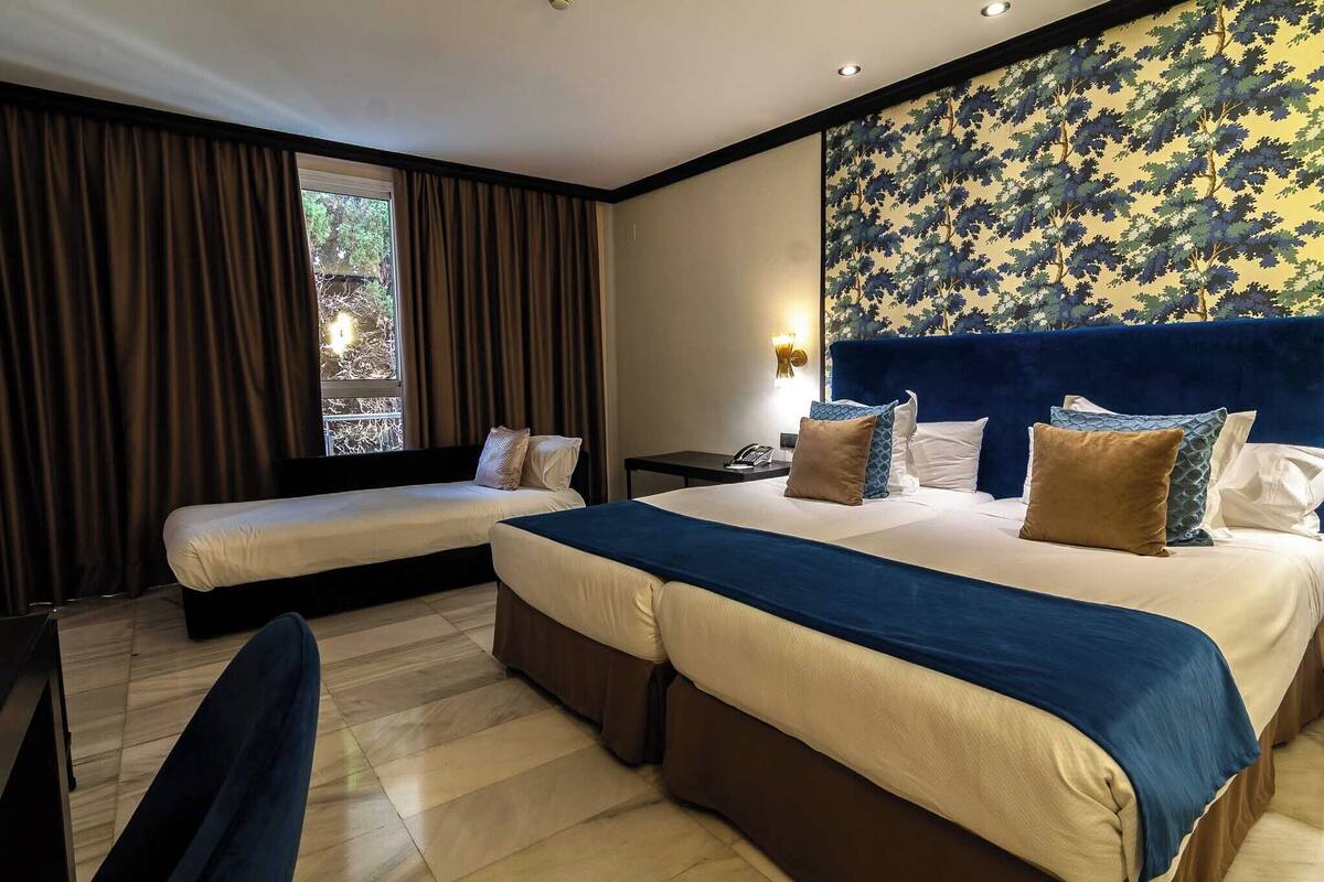Une chambre d’hôtel avec deux lits, un bureau et une fenêtre avec des rideaux.