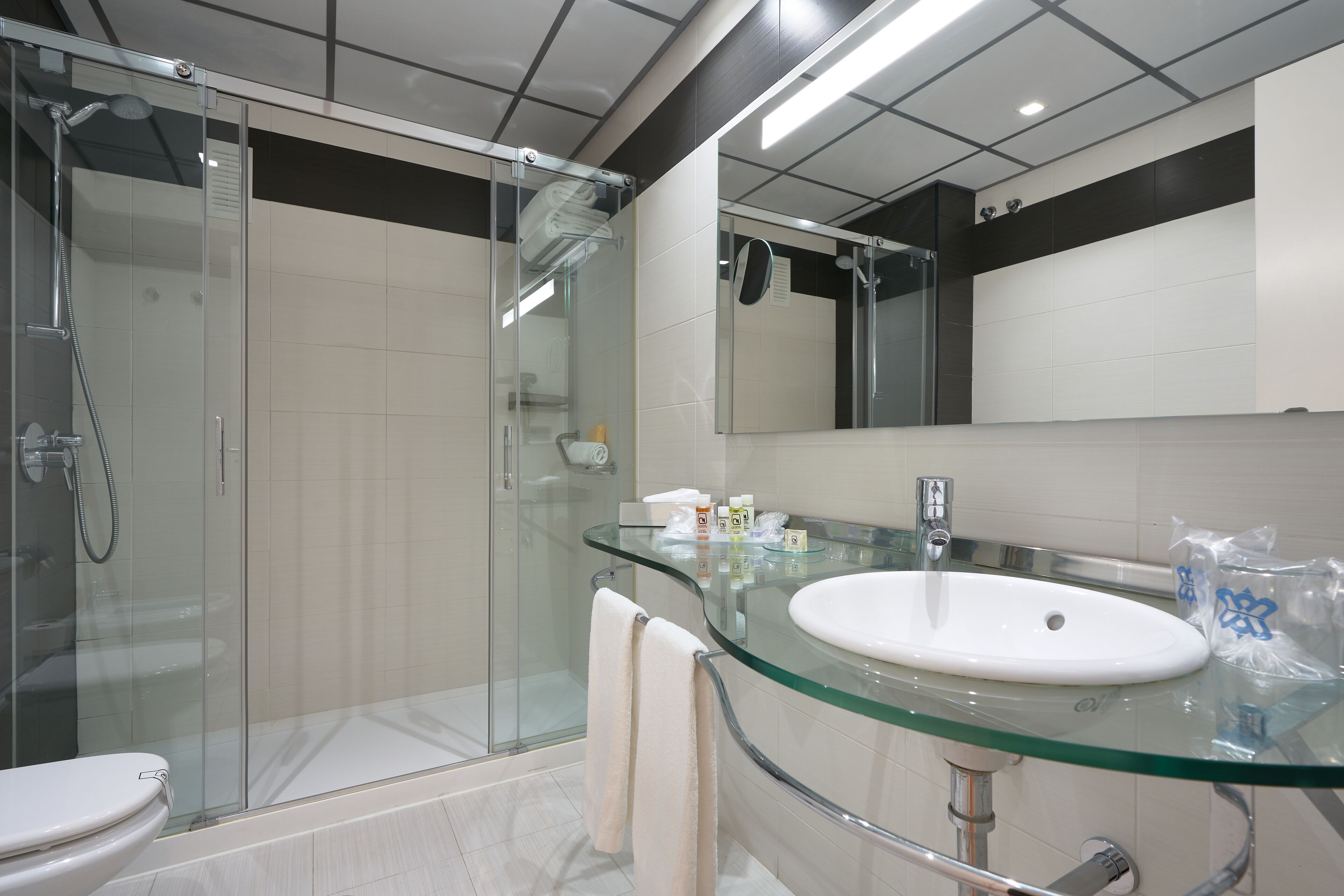 A modern bathroom with a glass shower enclosure, a glass sink, and a large mirror.