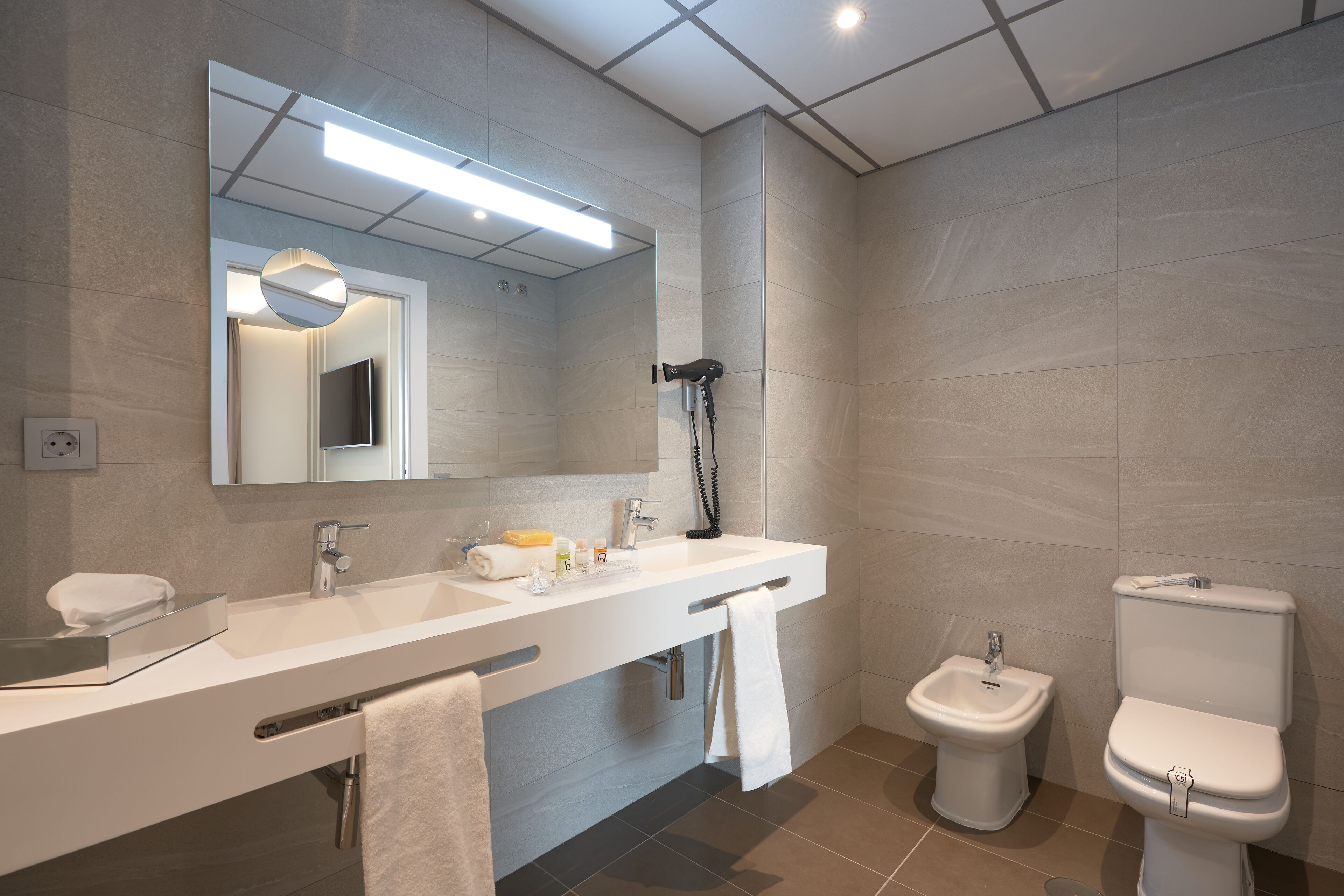 Un baño moderno con un tocador largo, un espejo, un secador de pelo, un bidé y un inodoro.