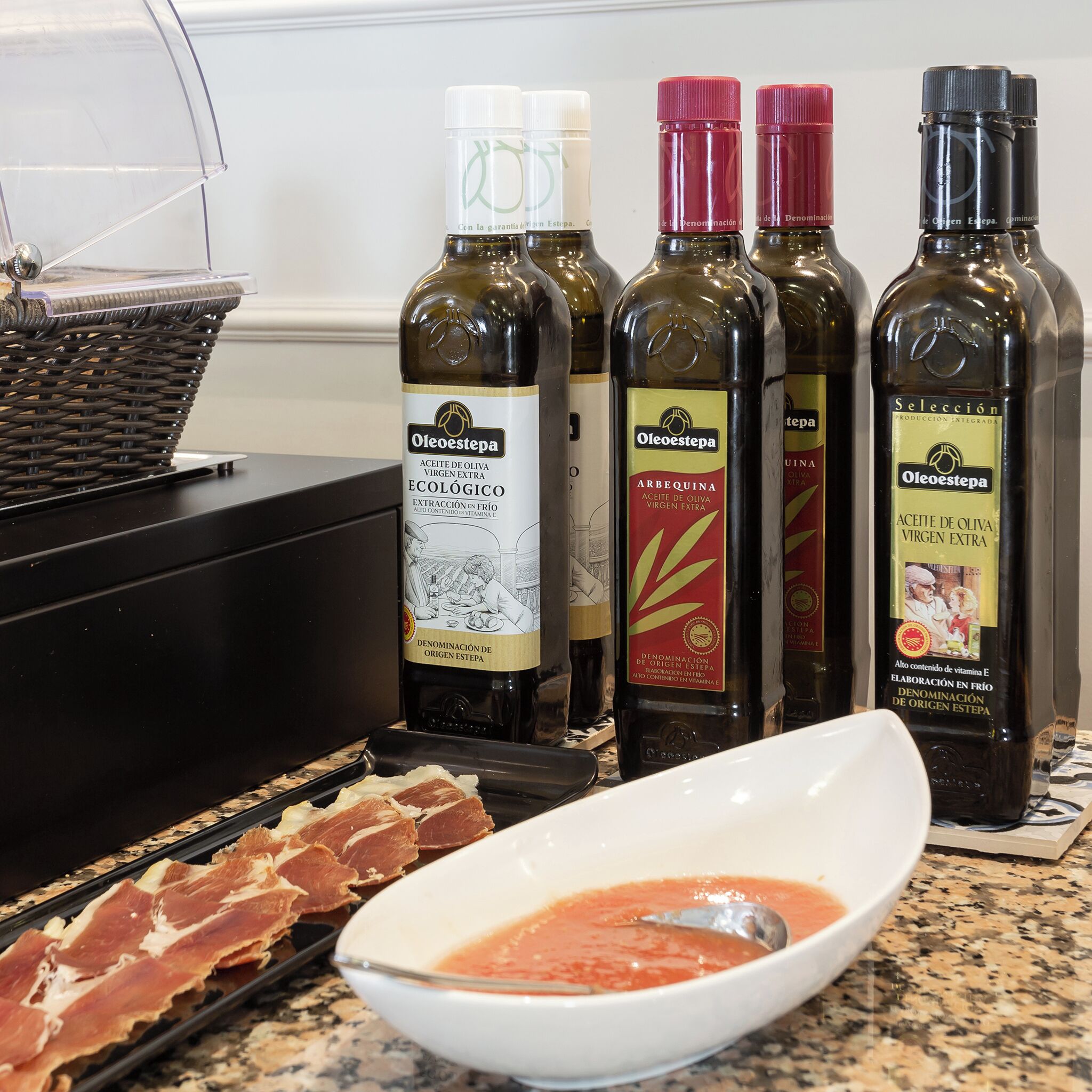 Bottles of olive oil, a bowl of tomato sauce, and sliced meats on a countertop.