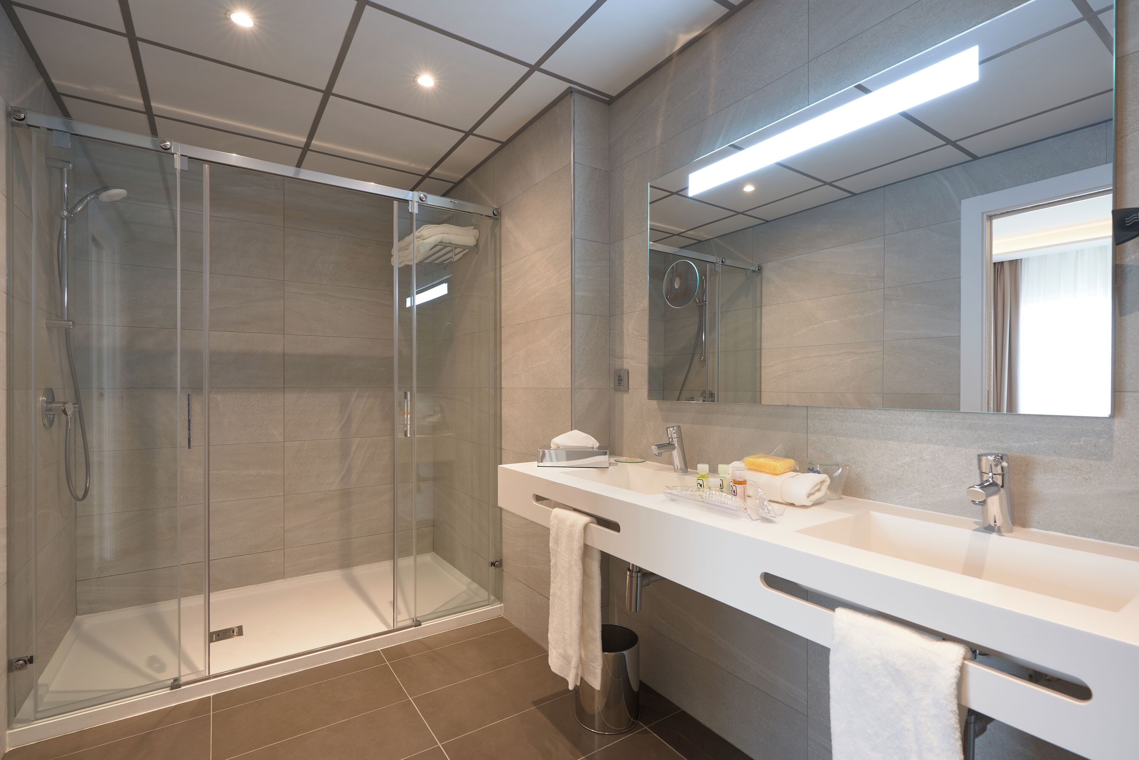 A modern bathroom with a glass-enclosed shower, a white sink, and a large mirror.