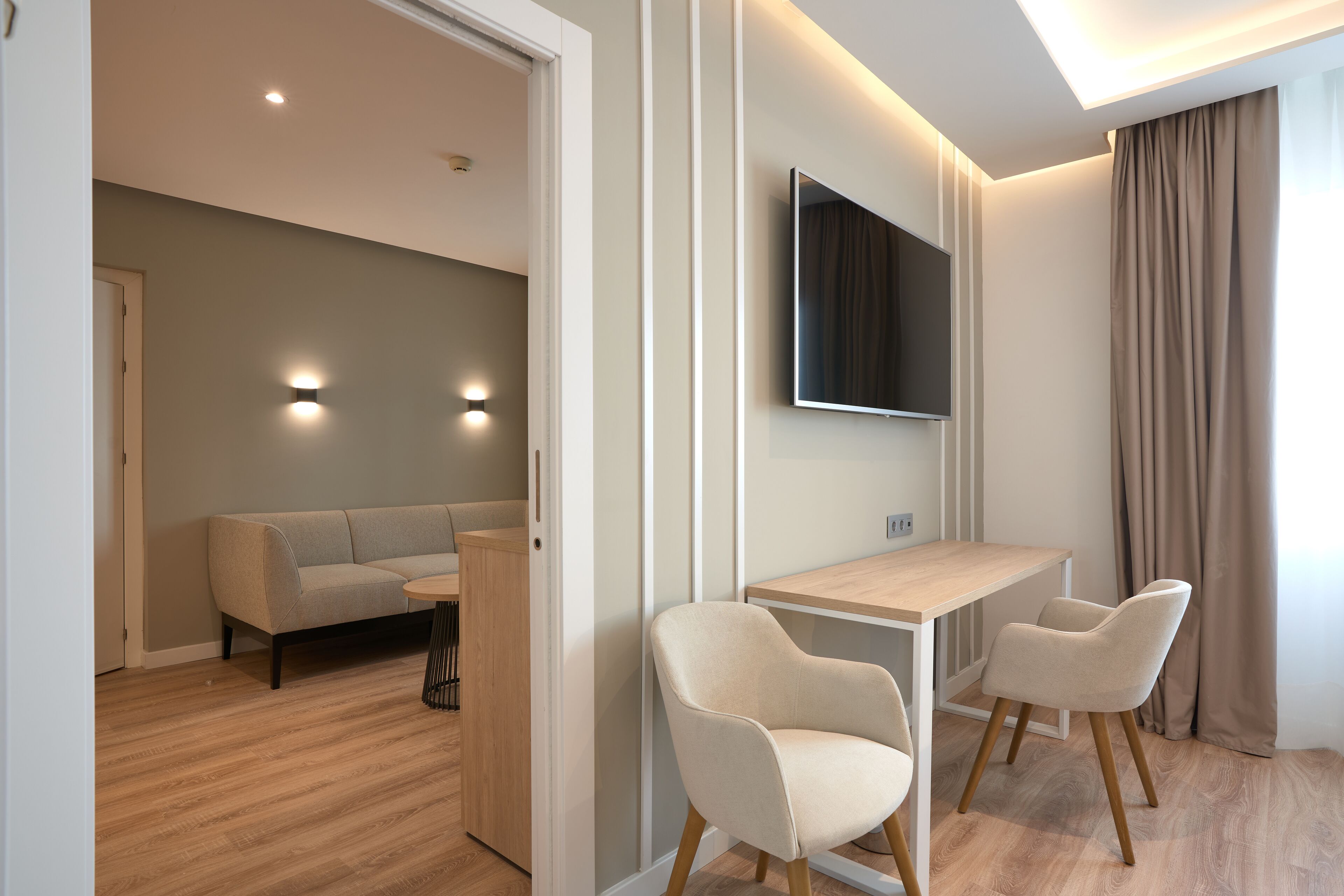 Una sala de estar moderna con un sofá, un televisor montado en la pared y un comedor con mesa y sillas.