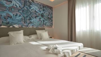A hotel room with a large bed, a headboard with a decorative panel, a bedside table, and a window with curtains.