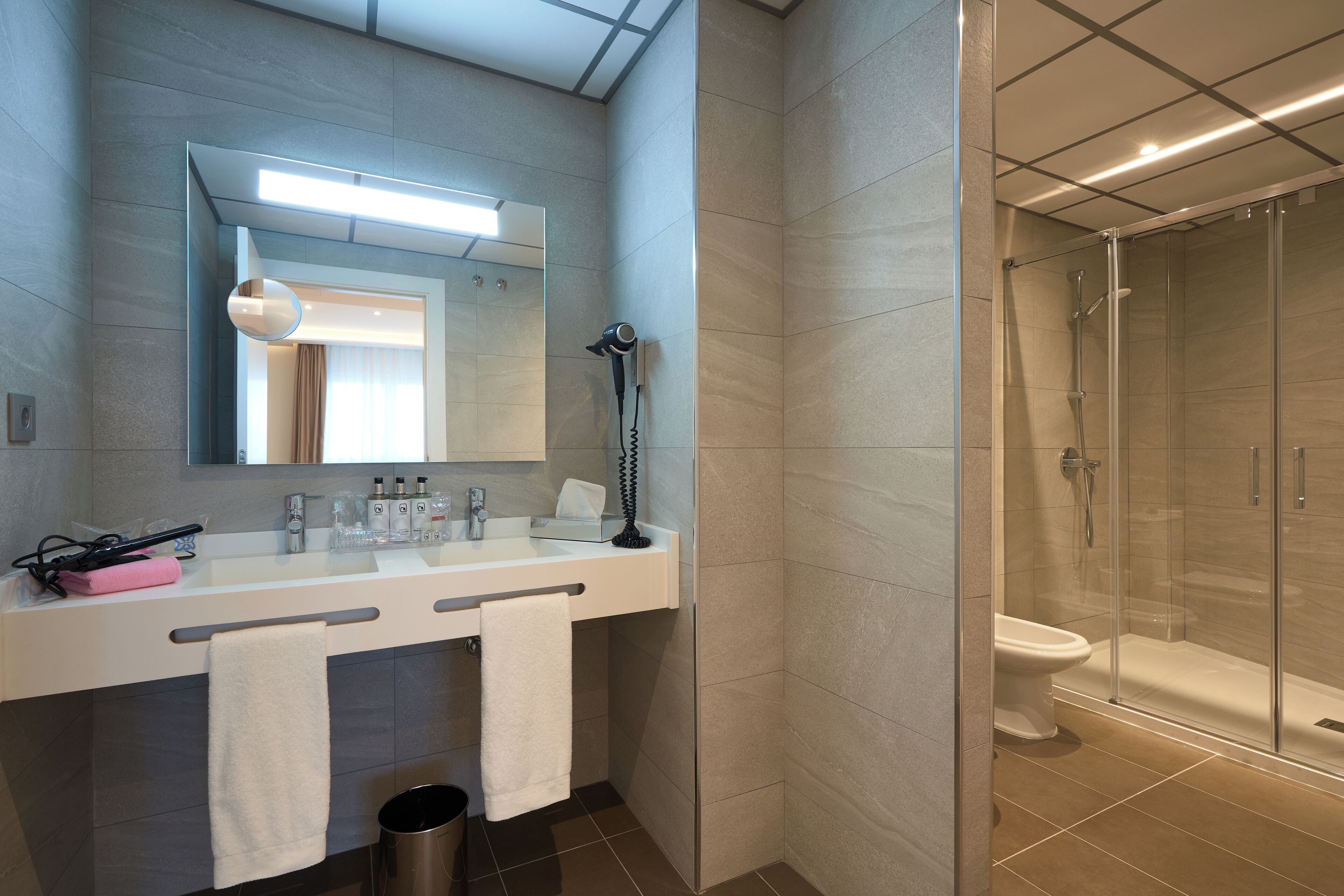 Een moderne badkamer met een grote spiegel, een witte wastafel en een douche met glazen wanden.