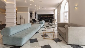 Un moderno vestíbulo de hotel con un sofá azul claro, un sofá beige y una mesa de centro geométrica.