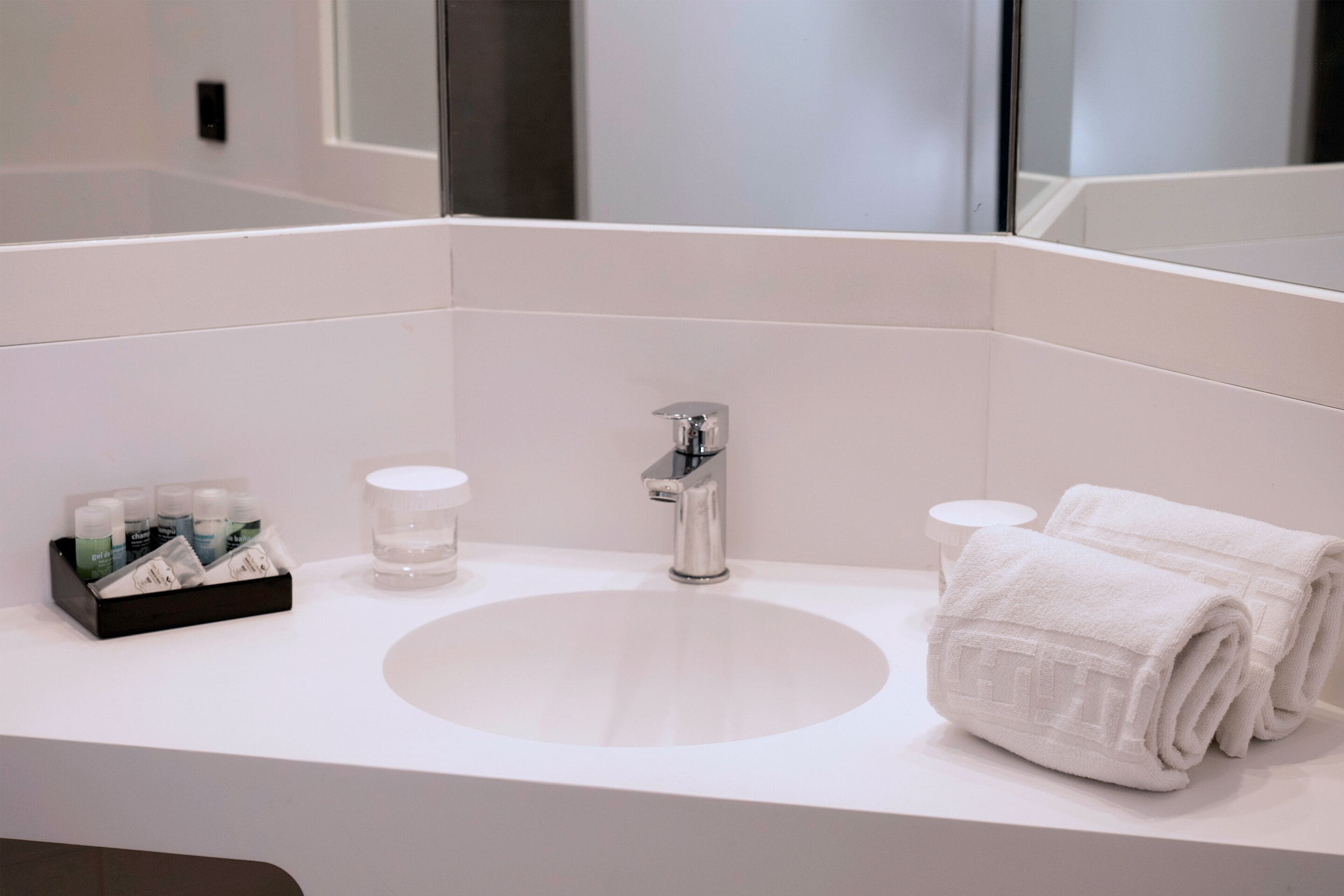 Un baño moderno con un lavamanos blanco, un espejo y toallas ordenadas.