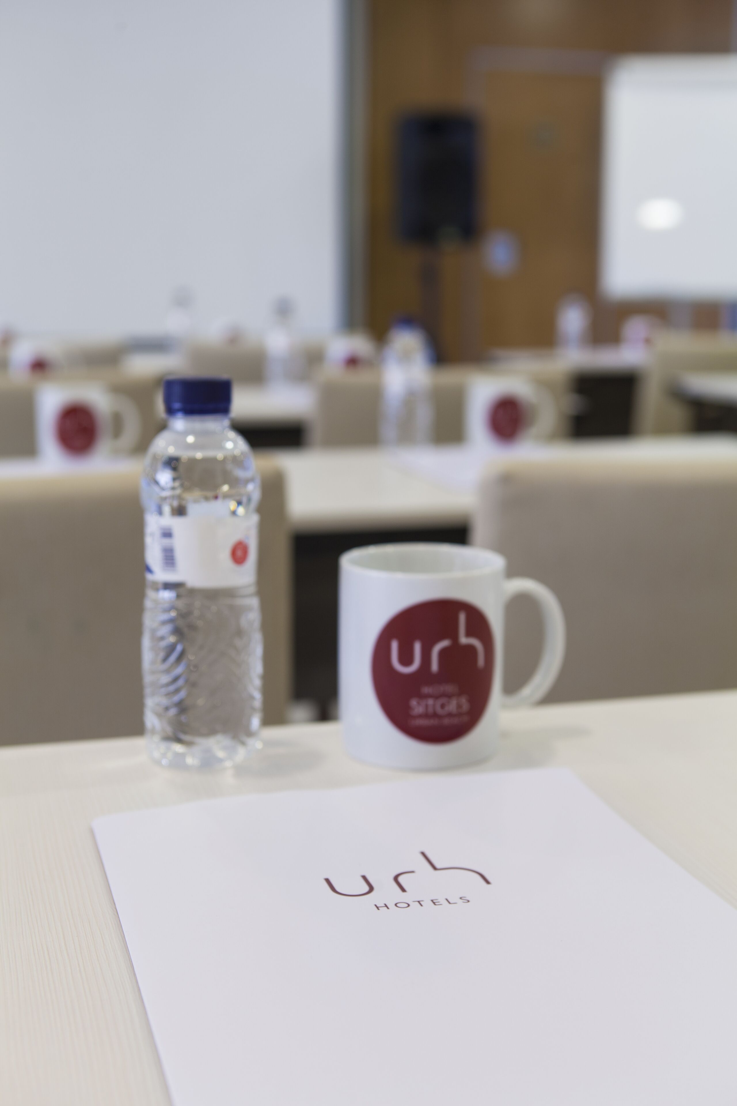 A conference room with a water bottle, a mug, and a nameplate with the logo "Urh Hotels".