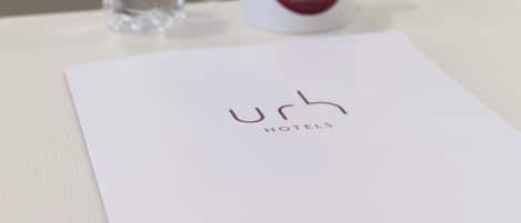 A conference room with a water bottle, a mug, and a nameplate with the logo "Urh Hotels".
