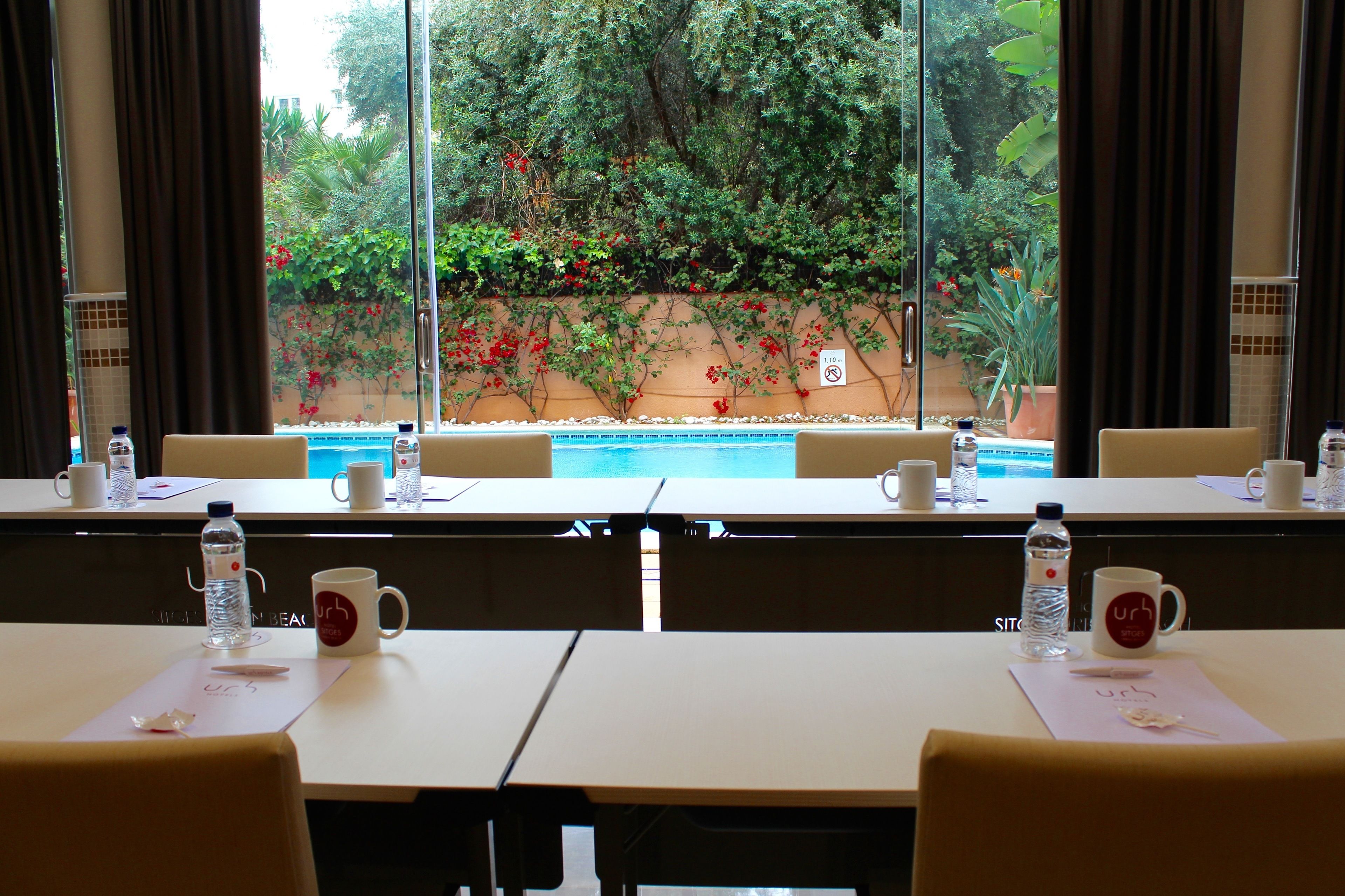 Un salón de conferencias con mesas, sillas y vistas a un jardín con piscina.