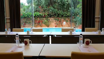 Un salón de conferencias con mesas, sillas y vistas a un jardín con piscina.