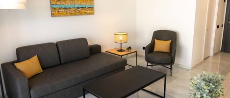A modern living room with a dark grey sofa, a black coffee table, a side table with a lamp, and a chair with a yellow cushion.
