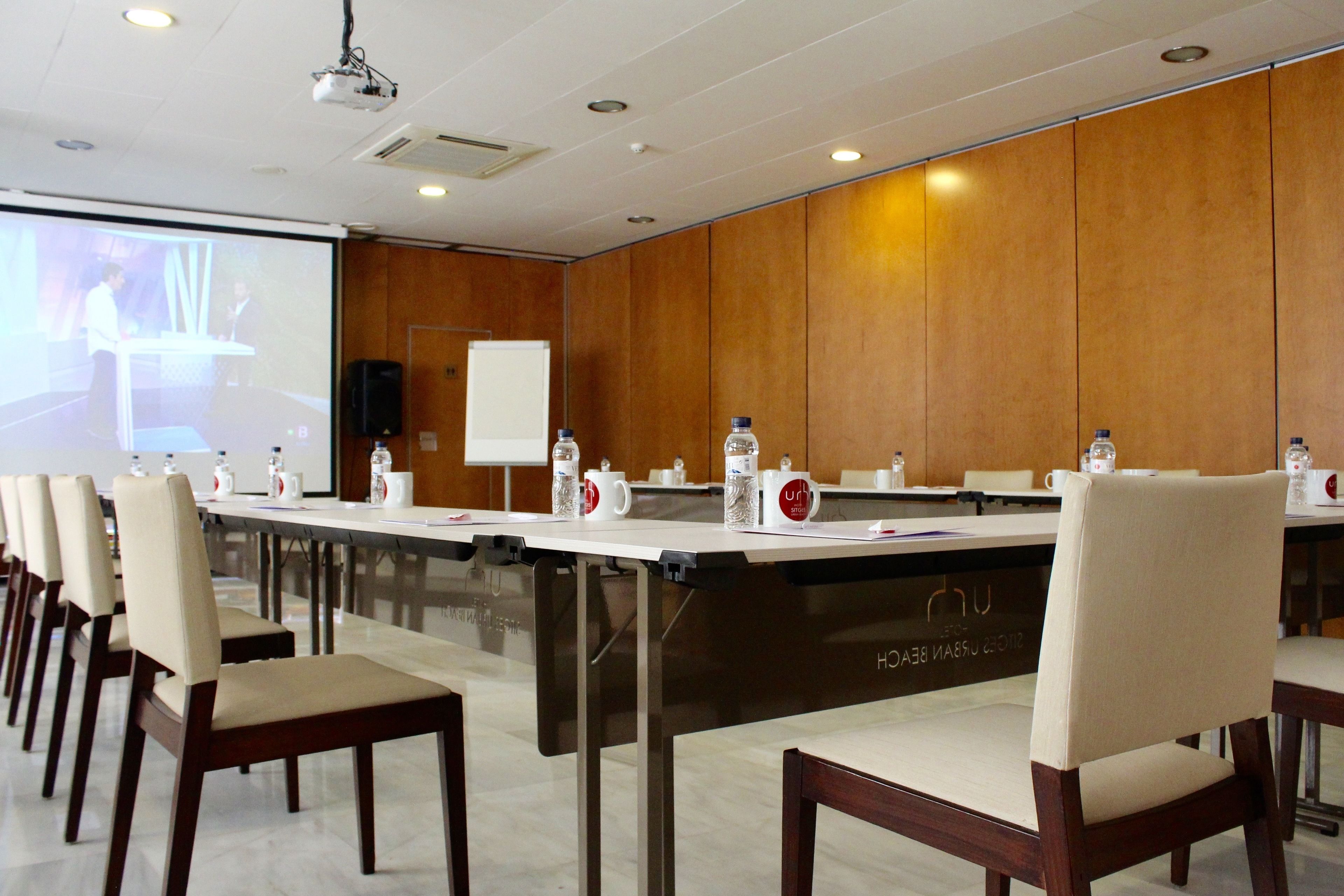 A conference room with a long table, chairs, a projector screen, and a whiteboard.