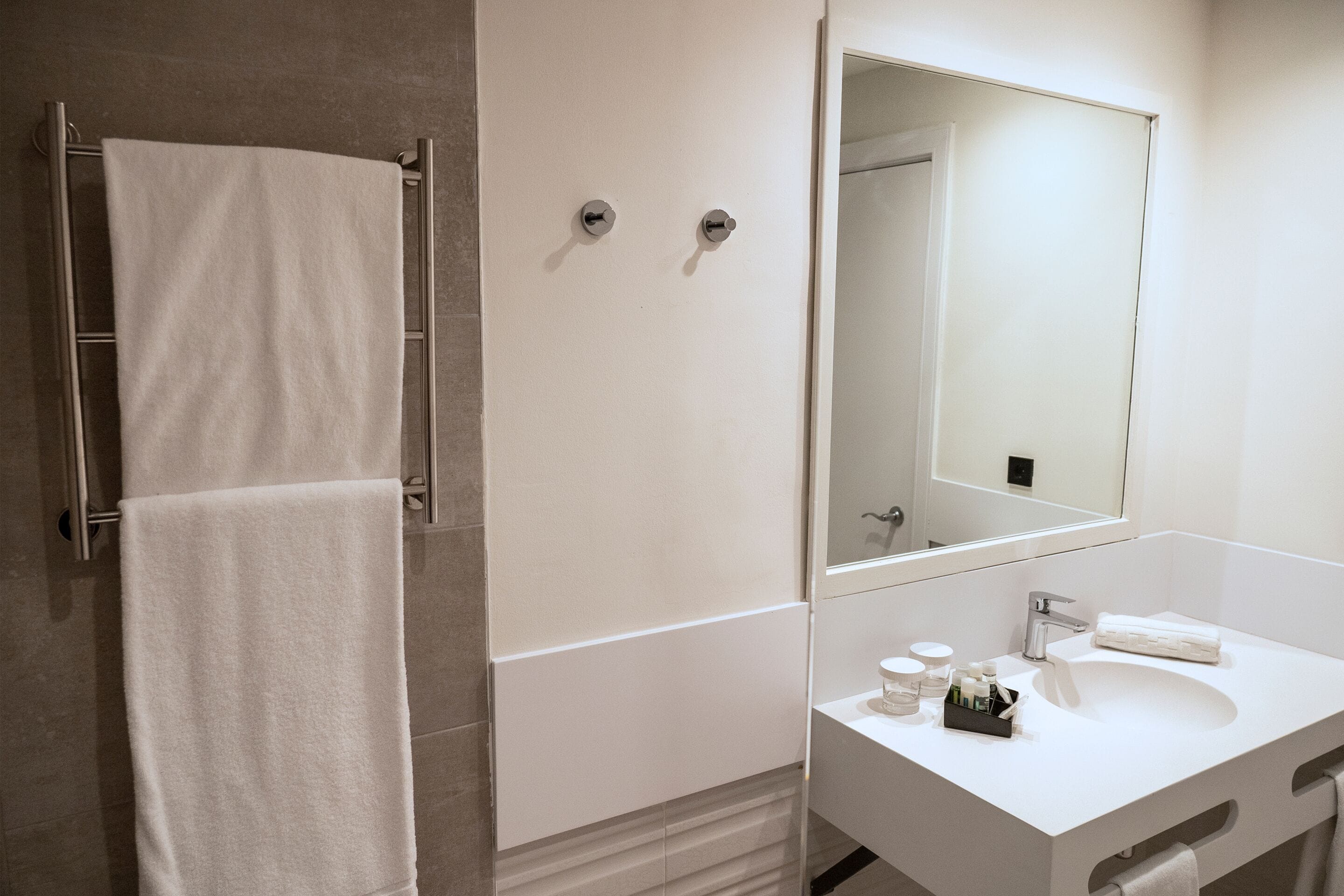 A modern bathroom with a white sink, mirror, and towel rack.